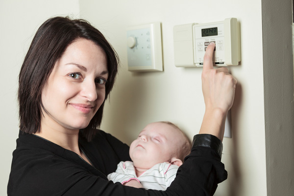 image of woman adjusting thermostat to turn on furnace