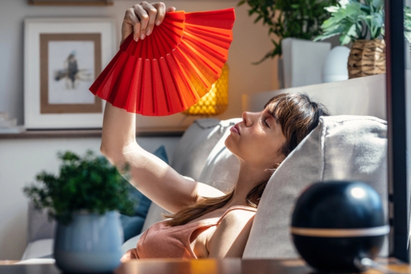 woman using hand fan indoors due to poor HVAC air flow