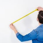 Rear view of man measuring wall with tape measure depicting sizing standby generator