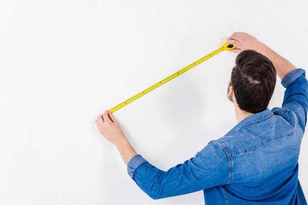 Rear view of man measuring wall with tape measure depicting sizing standby generator