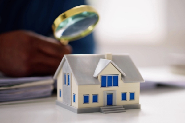 cropped view of a man's hand holding a magnifying glass while looking at a miniature house depicting Square Footage and Home Design