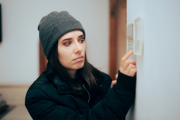 woman feeling cold at home checking the thermostat and furnace not heating