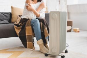 woman with blanket trying to keep warm with an electric space heater due to furnace malfunction