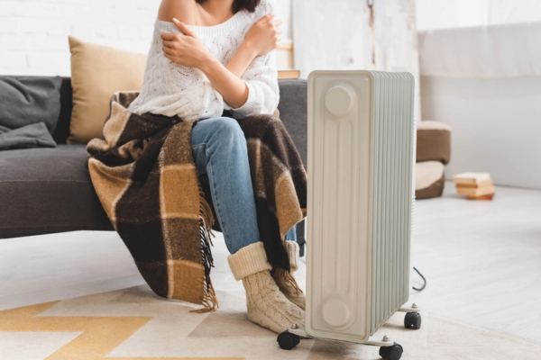 woman with blanket trying to keep warm with an electric space heater due to furnace malfunction