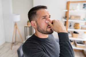 woman plugging nose due to smelly odors at home