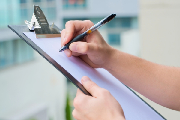 cropped view of a man's hand holding a clipboard and a pen depicting Maintaining & Monitoring Double-Wall Heating Oil Tanks