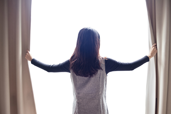 image of homeowner opening curtains to let sun in during winter for home heating