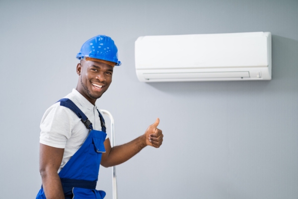 smiling HVAC technician doing a thumbs up beside a ductless AC