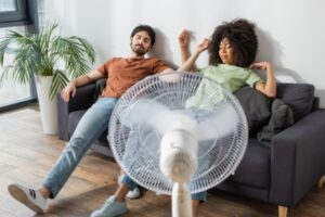 couple feeling warm and exhausted in front of an electric fan due to AC not keeping up