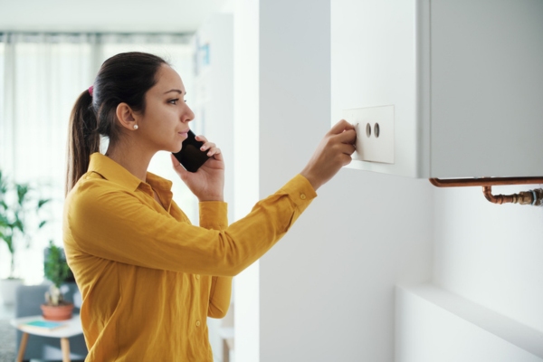 woman on the phone while turning on boiler at home