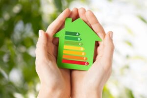 Hands holding green paper house with energy efficiency chart depicting AFUE & AFUE2
