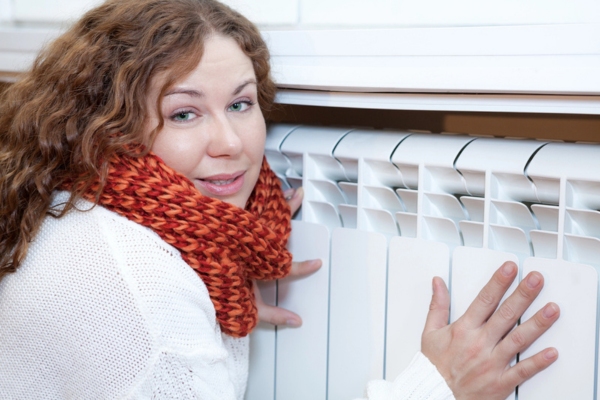 woman trying to stay warm near the heating radiator due to cold spots in the house