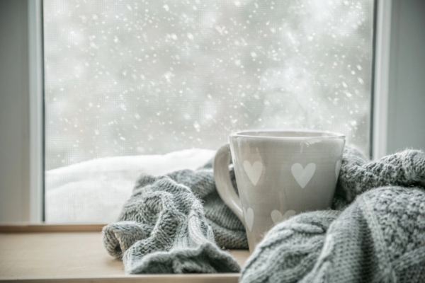 hot chocolate in a mug wrapped in a scarf by the window during snow