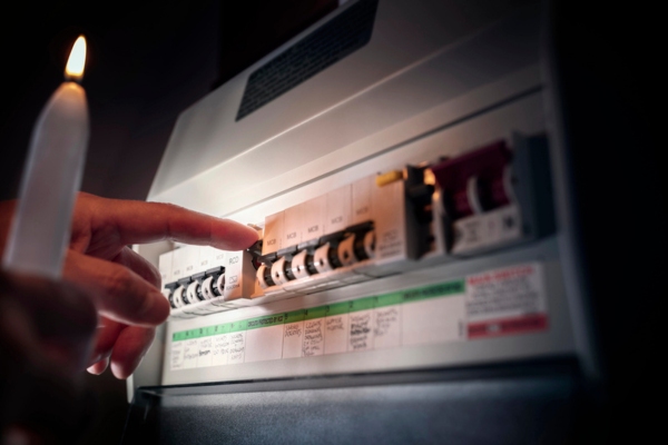 homeowner holding candle checking electric fuse box due to blackout