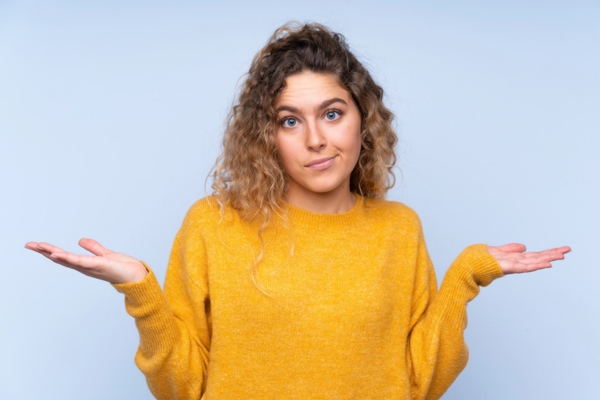 woman in a mustard colored sweater shrugging depicting Steps to Take When Rising Heating Costs Create Financial Concern