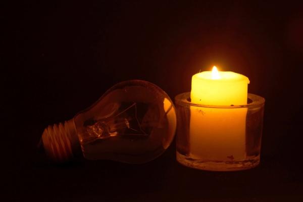 burning candle beside a lightbulb depicting power outage