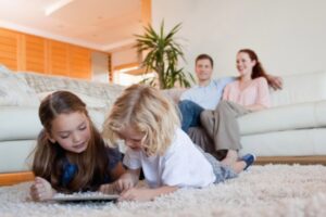 Children using smart tablet on the carpet and parents watching TV depicting comfortable at home due to air conditioner