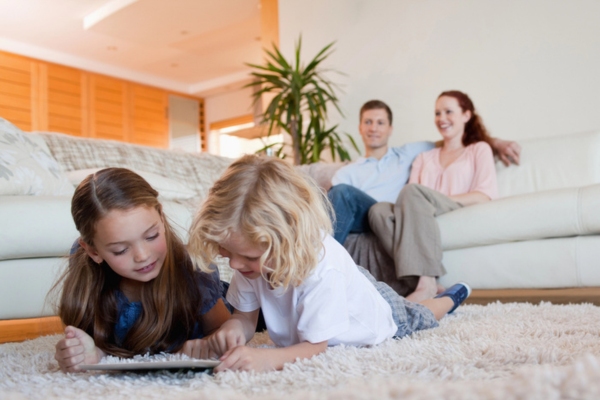 Children using smart tablet on the carpet and parents watching TV depicting comfortable at home due to air conditioner
